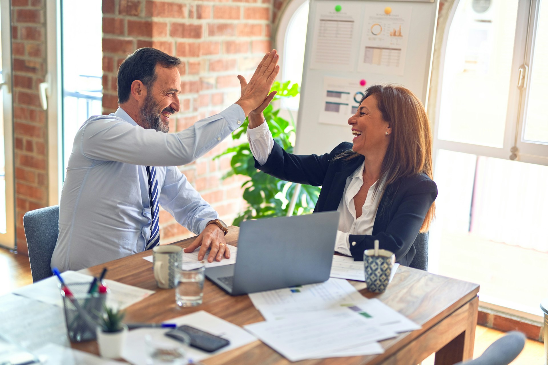 Two business professionals high-fiving each other at a desk, celebrating a successful collaboration or achievement.